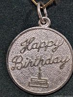 Close-up front view of the round silver pendant showing 'Happy Birthday' text and cake relief.