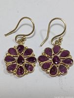Pair of ruby floral silver earrings laid flat showing one earring face up and the other with hook visible