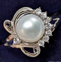 Close-up front view of silver ring with large freshwater pearl center surrounded by clear cubic zirconia stones and decorative silver swirls on the band.