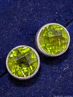 Close-up front view of both round green peridot quartz earrings in silver bezel settings on blue cloth.