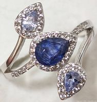 Close-up angle of the silver ring with the three pear-shaped stones highlighted from above, showing the dark blue center stone and two lighter stones with surrounding small clear stones.