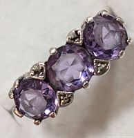 Close-up photo showing side angle view of silver ring with three purple amethyst stones held by prongs and separated by small decorative silver elements.