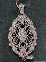 Front view of oval sterling silver pendant with cubic zirconia stones, showing detailed filigree design and stone arrangement.