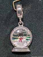 Front view of snow globe charm showing snowman, trees and clear dome set in silver frame with clasp