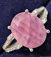 Close-up of silver ring with oval pink ruby CZ and decorative band with clear stones.