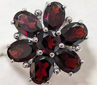 Close-up of the silver ring showcasing seven faceted garnet stones arranged in a flower shape with detailed silver prongs.