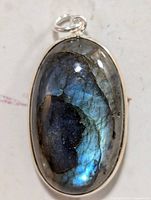 Front view of oval labradorite pendant with reflective blue iridescence and silver bezel setting.