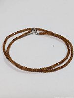 Full view of the brown gemstone necklace coiled on white surface.