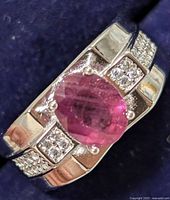 Close up angled view of silver ring with oval ruby CZ center stone and small accent cubic zirconia stones on band