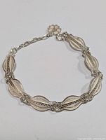 Full view of the silver bracelet laid flat showing the linked leaf-shaped decorative elements and chain extender with flower charm.