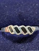 Close-up photo of silver ring showing geometric cut-out design on top, placed against dark blue background.