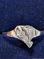 Front view of silver ring size 8 showing abstract irregularly shaped face with textured detail on a dark fabric background.