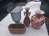 Group shot of four outdoor containers: metal basket, red & cream urn, tribal design vase, rectangular planter