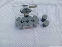 Ten labelled grey film canisters inside clear plastic box on cloth backdrop