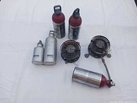 Overall view of two stoves, three red Coleman bottles, two silver SIGG bottles