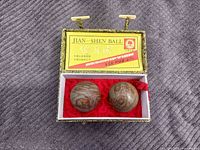 Open brocade box showing two marble balls seated in red lining