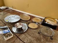 Wide view of platters, chargers, napkin rings arranged on floor showing variety and condition