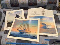 Three nautical art prints laid out on a couch with a note indicating two are signed and measurements about 20x25 inches.