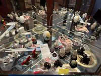 Wide shot of the collection showing metal foo dogs, ceramic hens, chopsticks with rests, glass miniature display cases, and wooden stands all arranged inside a glass cabinet.