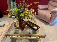 Brown vase with yellow faux flowers, dark narrow wall shelf, and plastic framed instrument panel on glass table with beige carpet and red wall background