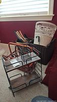 Photo showing wood and metal two-tier shelf, wood magazine rack, dark rectangular basket, reddish woven basket, tall white round basket, and wooden hangers