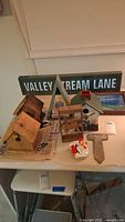 Wide view of assorted bird houses, street sign, memory cross, sound magnet, and decorative items on a table