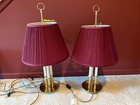 Pair of brass table lamps side by side on carpet with burgundy wall background, showing overall shape and design