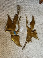Two brass style bird wall hangings laid flat on carpet, showing their full shape and detailed feather design.