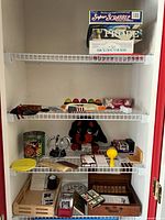 Photo of multiple board games including Super Scrabble Deluxe Edition, Probe, How to Host a Murder, The Last Train from Paris on top shelf. Middle and bottom shelves have plush toy dog, game components, poker chips, card accessories, and dominoes boxed set