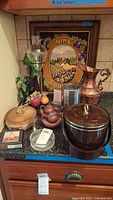 Overview of all items showing central ceramic lidded bowl, two dragon tea pitchers, Lenox wine chiller, ice bucket, decorative fruit, wine county wall art in frame, and coasters.