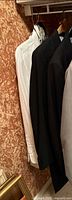 Multiple formalwear garments including tuxedo pants and dress shirts on hangers