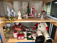 Shelving unit with Lenox nutcracker and various Christmas ceramic and plush decorations, fabric tree skirts visible below