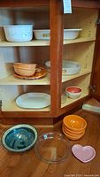 Cabinet shelf with various Corning, Gibson, and other bowls arranged inside and on the counter including orange bowls, a floral Corning dish, and a Pyrex pie plate