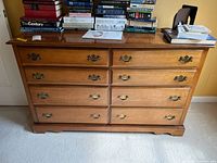 Front view of dresser showing eight drawers, multiple books on top, wooden finish, brass handles.
