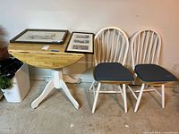 Wooden drop leaf table with two spindle back chairs, and framed pictures on table