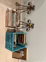 Photo showing assortment of wood and metal photo frames stacked inside a blue crate plus a few placed on the floor, along with two decorative metal easels against the wall.