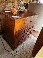 Side view of the wood end table with decorative cabinet doors and drawer on top.