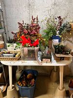 Table with various faux flowers, foliage, ribbons, and floral supplies arranged on top, with a large blue tub underneath containing more faux flowers.