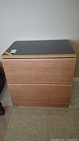 Front view of the two-drawer wooden file cabinet with black top surface, showing overall condition and design.