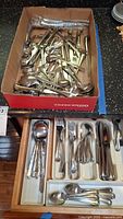Photo showing multiple spoons, forks, and knives; flatware stored in box and drawer organizer.