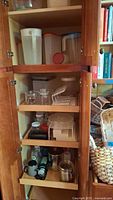 Multiple Rubbermaid and plastic food storage containers, pitchers, jars, and canisters on cabinet shelves alongside other kitchen items.