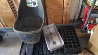 Wide view showing black garden cart, black seedling trays, and clear plastic compartment organizer on floor