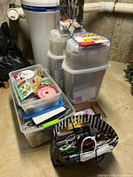 Wide view of multiple stacked plastic storage bins filled with gift wrap supplies, ribbons, cards, and gift bags stored in basement.