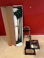 Four golf clubs with protective headcovers in box, pushed against red wall with carpeted floor.
