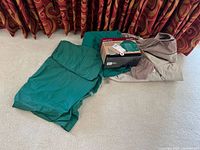 Three greenish grill covers laid on floor along with a boxed grill cover and a metal utensil with wooden handle.