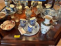 Wide view of handpainted ceramic teacups, pitchers, vase, bowl, and etched glass stemware on wooden table