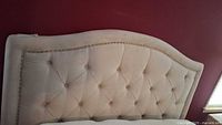 Front view of beige cloth headboard with button tufting and curved top edge against a red wall.