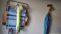 Foldable beach chair in blue and white stripes hanging on wall with two packaged kites and part of umbrellas visible.