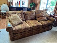 Front view of three cushion sofa with three decorative pillows on a hardwood floor near windows and furniture.
