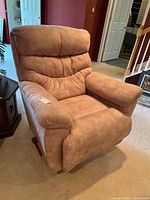 Front and side angle view of tan suede-like La-Z-Boy recliner chair showing padded backrest and arms; chair is in a carpeted room near stairs.